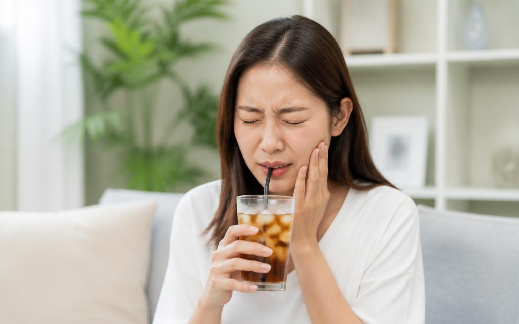 Person wincing with sensitivity while drinking an iced drink
